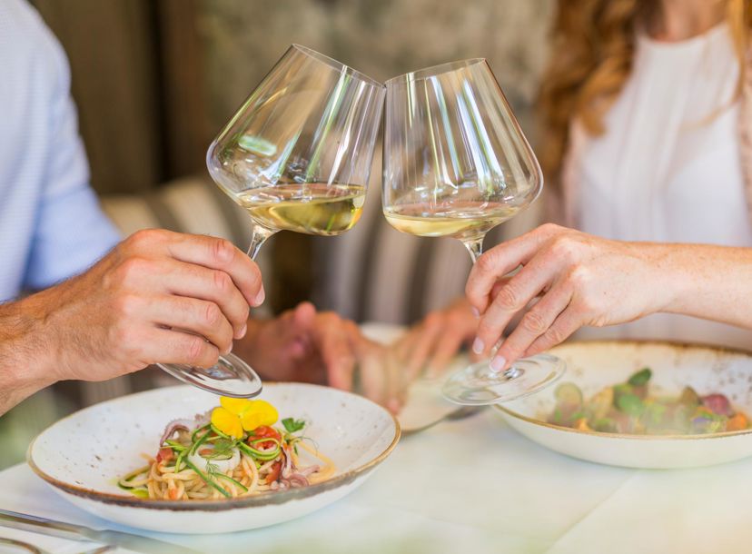 Two people are clinking their white wine glasses during a meal at a restaurant